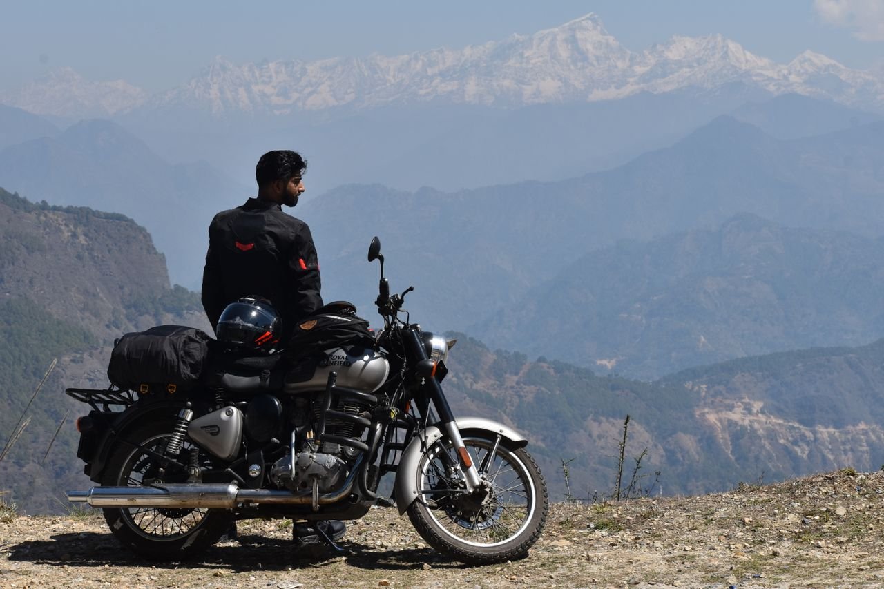 A motorcyclist with a Royal Enfield on a mountain road in Pithoragarh, Uttarakhand, enjoying the Himalayan view.
