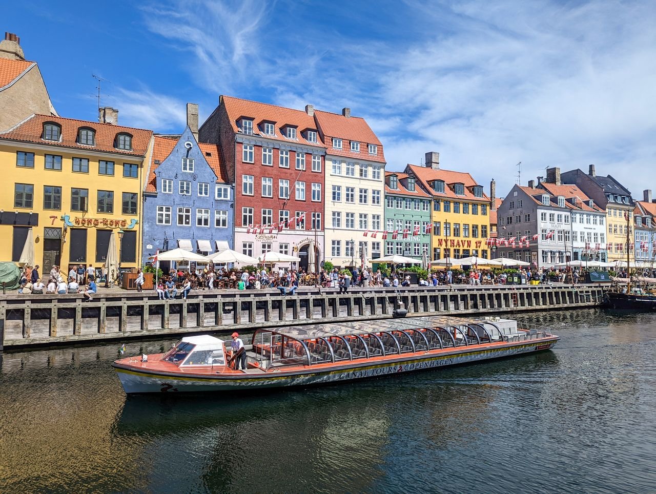 Vibrant canalside view of Nyhavn's colorful historic houses and tourist boats in Copenhagen, Denmark.